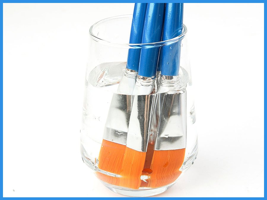 Close-up of flat paint brushes with blue handles soaking in a glass of water