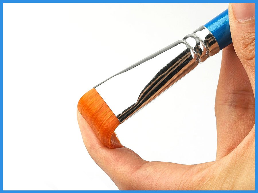 Close-up of a flat paint brush with orange synthetic bristles held by a hand against a white background.