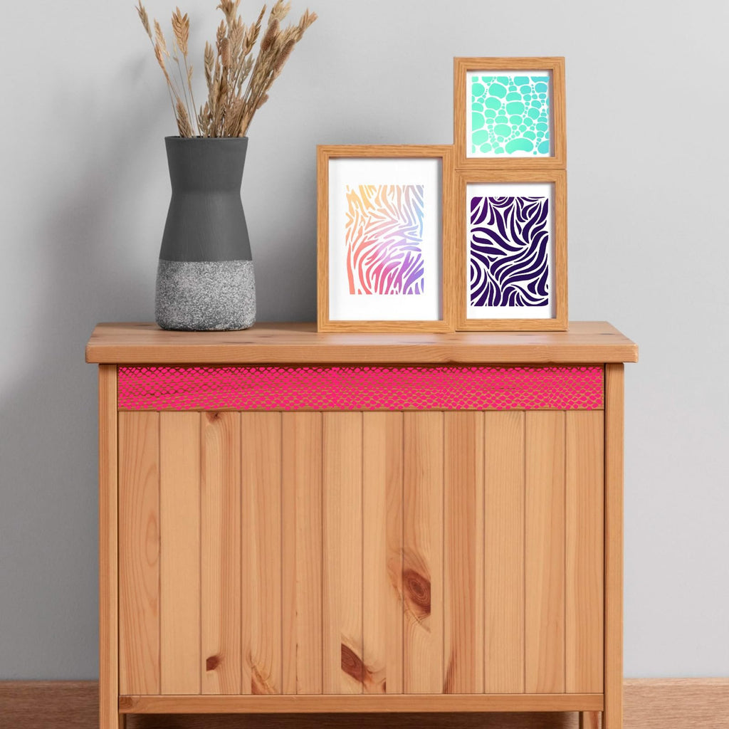 Three framed art prints with abstract patterns displayed on a wooden cabinet next to a vase of dried grass.
