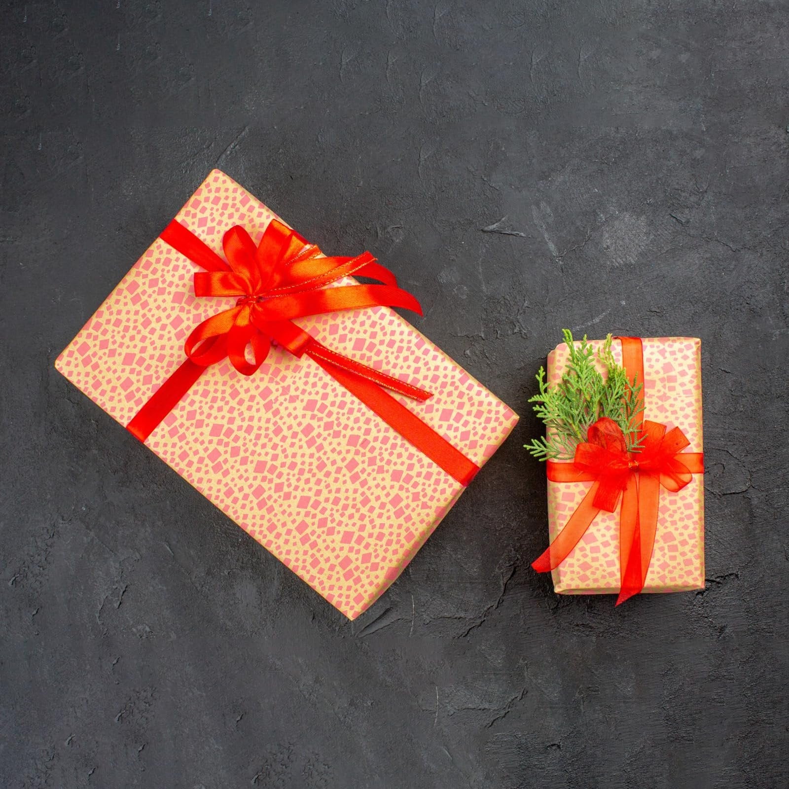Two gift boxes with red ribbon and green sprigs on a dark textured background, top-down view.