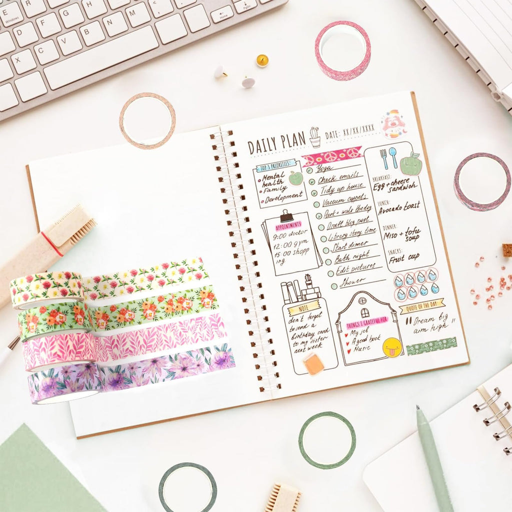 Stack of floral washi tape rolls next to an open daily planner on a desk with a keyboard.