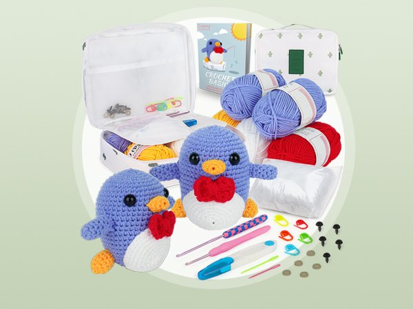 Crochet kit with yarn, crochet hooks, stuffing, and two finished penguin toys.