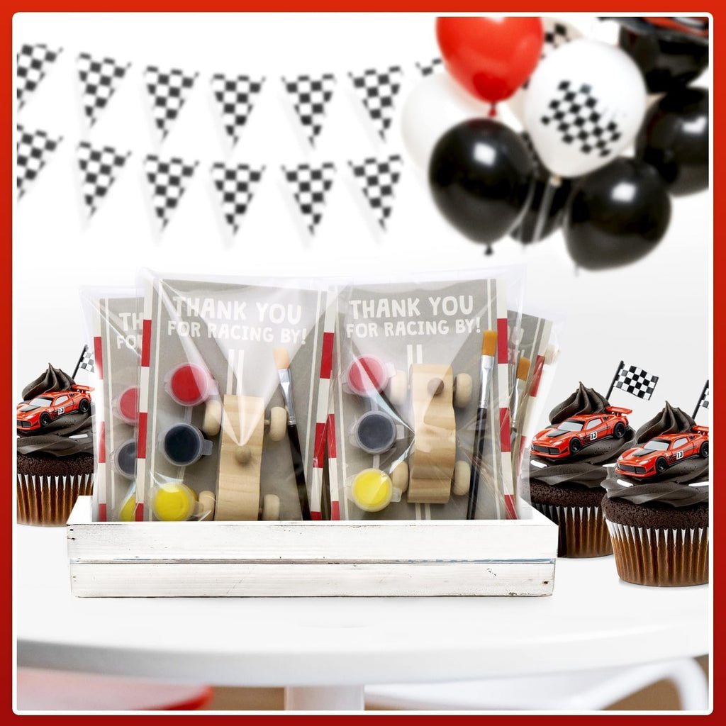 Unfinished wooden race car painting kits with paint and brushes, displayed with cupcakes and party decorations.