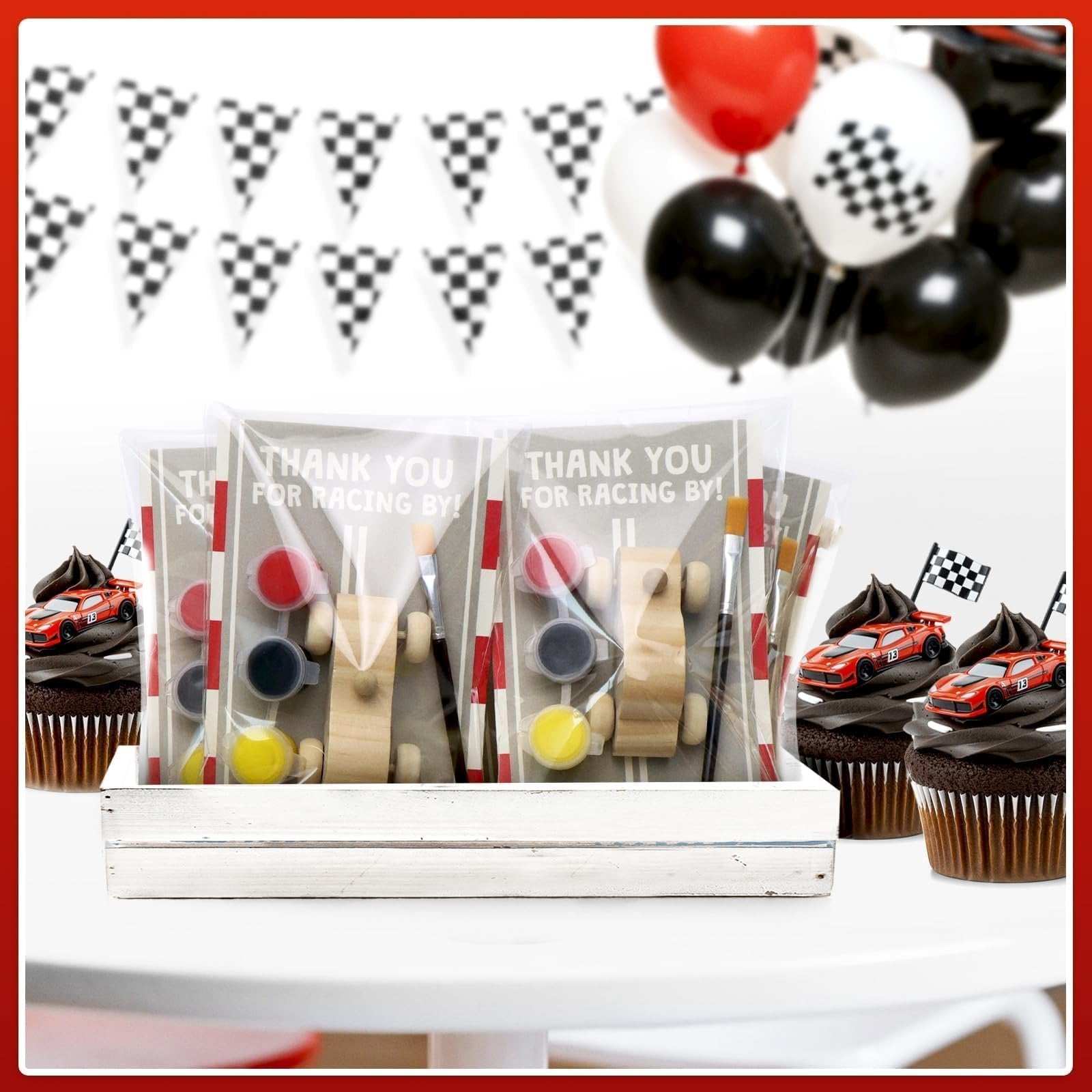 Unfinished wooden race car painting kits with paint and brushes, displayed with cupcakes and party decorations.