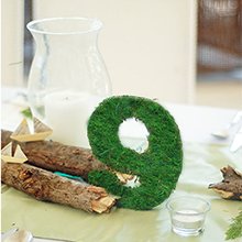 Green moss-covered number 9 decoration on a table with logs and a candle