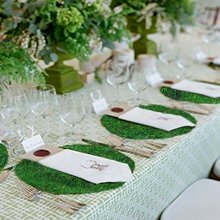 Table setting with green moss placemats, white napkins, and floral arrangements.