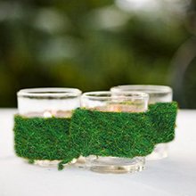 Three glass votive holders wrapped in preserved green moss, with a blurred green background.