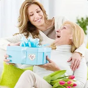 Woman receiving a light blue gift box with a bow from another woman, with tulips in the foreground.