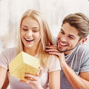Smiling couple, woman opening a gold gift box, man looking on happily