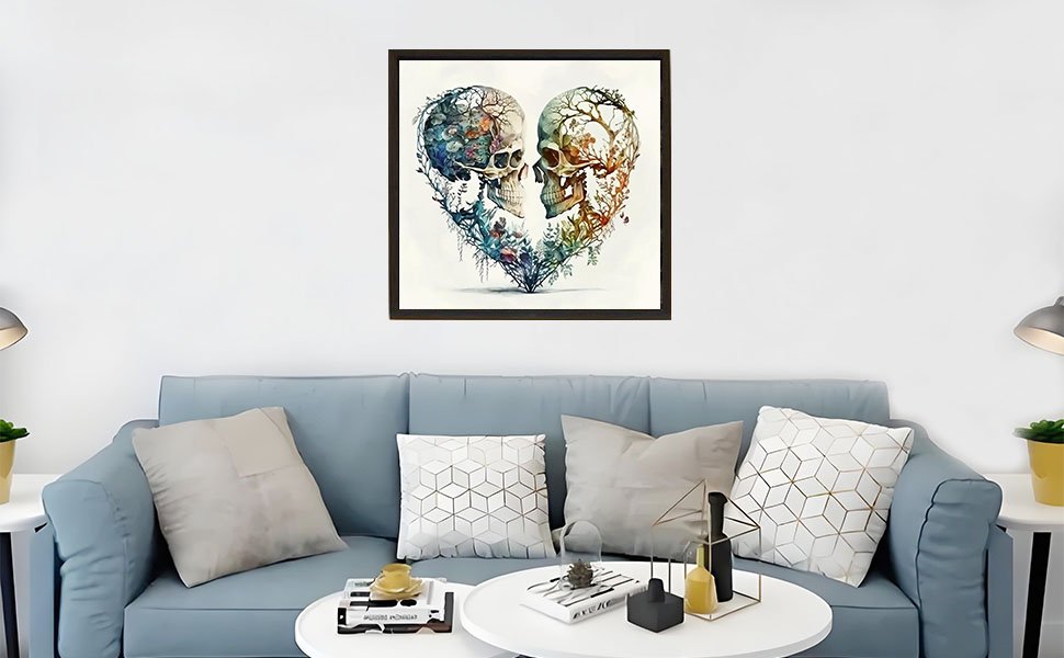 Framed heart-shaped diamond painting of two skulls intertwined with floral elements, displayed above a sofa.