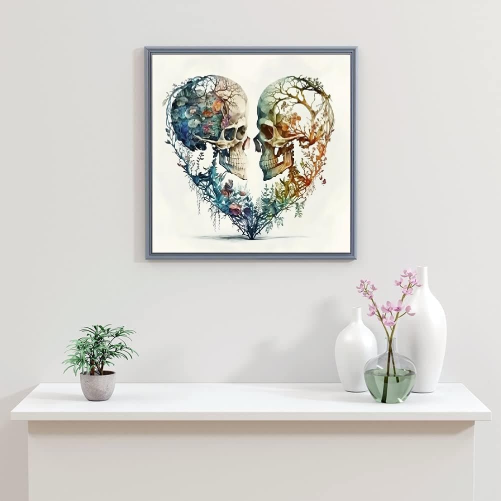 Framed diamond painting of two skulls forming a heart shape, decorated with colorful foliage and branches.