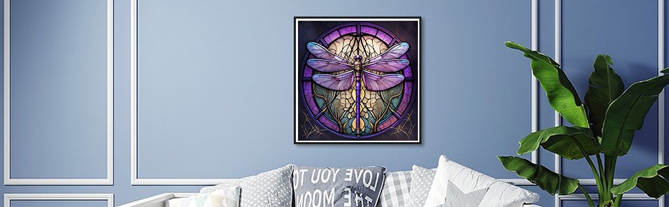 Dragonfly diamond painting artwork framed on a blue wall above a sofa with pillows and a plant.