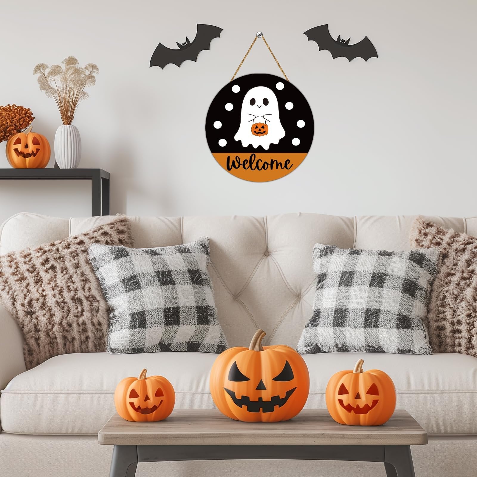 Round Halloween welcome sign with a ghost and pumpkin hanging above a couch with pumpkins on a coffee table.