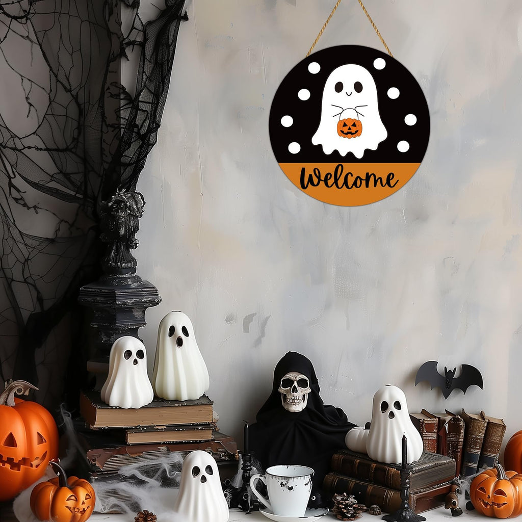 Round Halloween welcome sign with a ghost holding a pumpkin, hanging on a wall with spooky decorations.