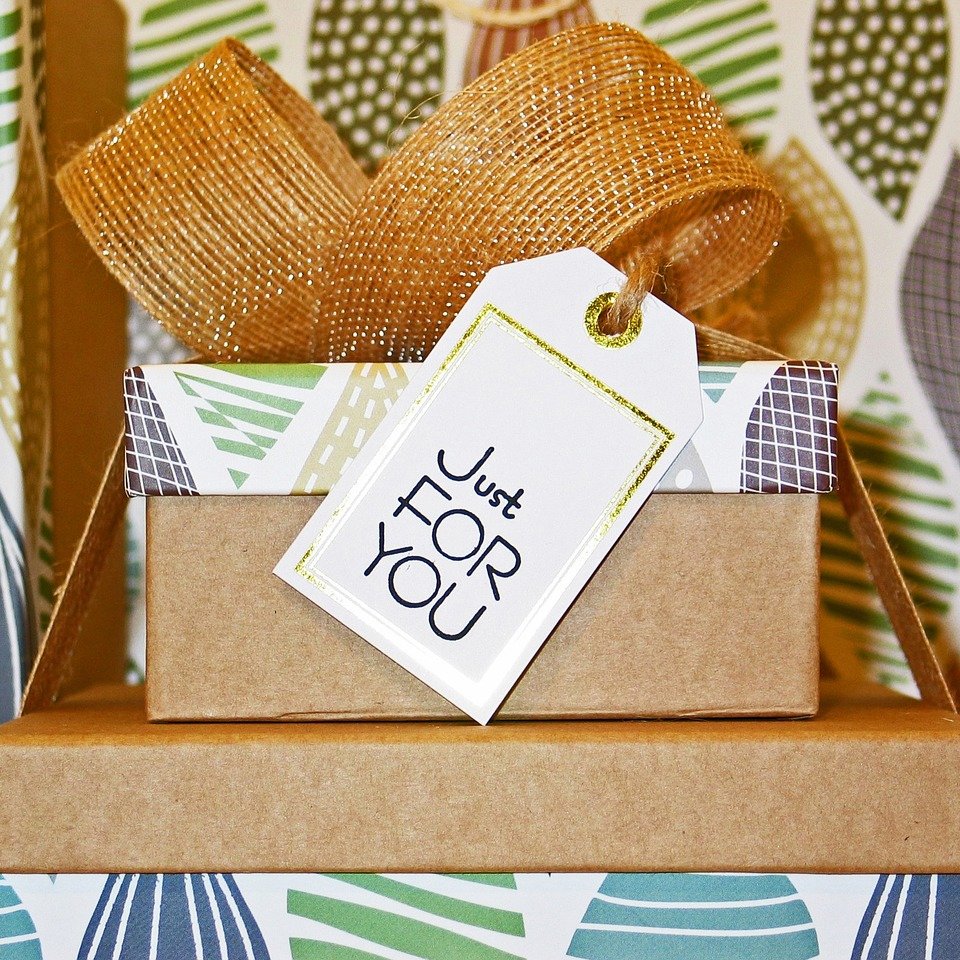 Gift box with a large golden bow and a 'Just For You' gift tag, set against a patterned background.