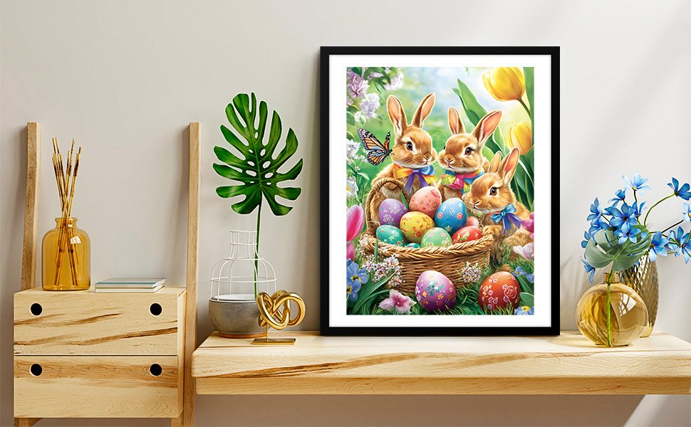 Framed diamond painting kit featuring three bunnies in a basket of Easter eggs, set on a shelf with decor.