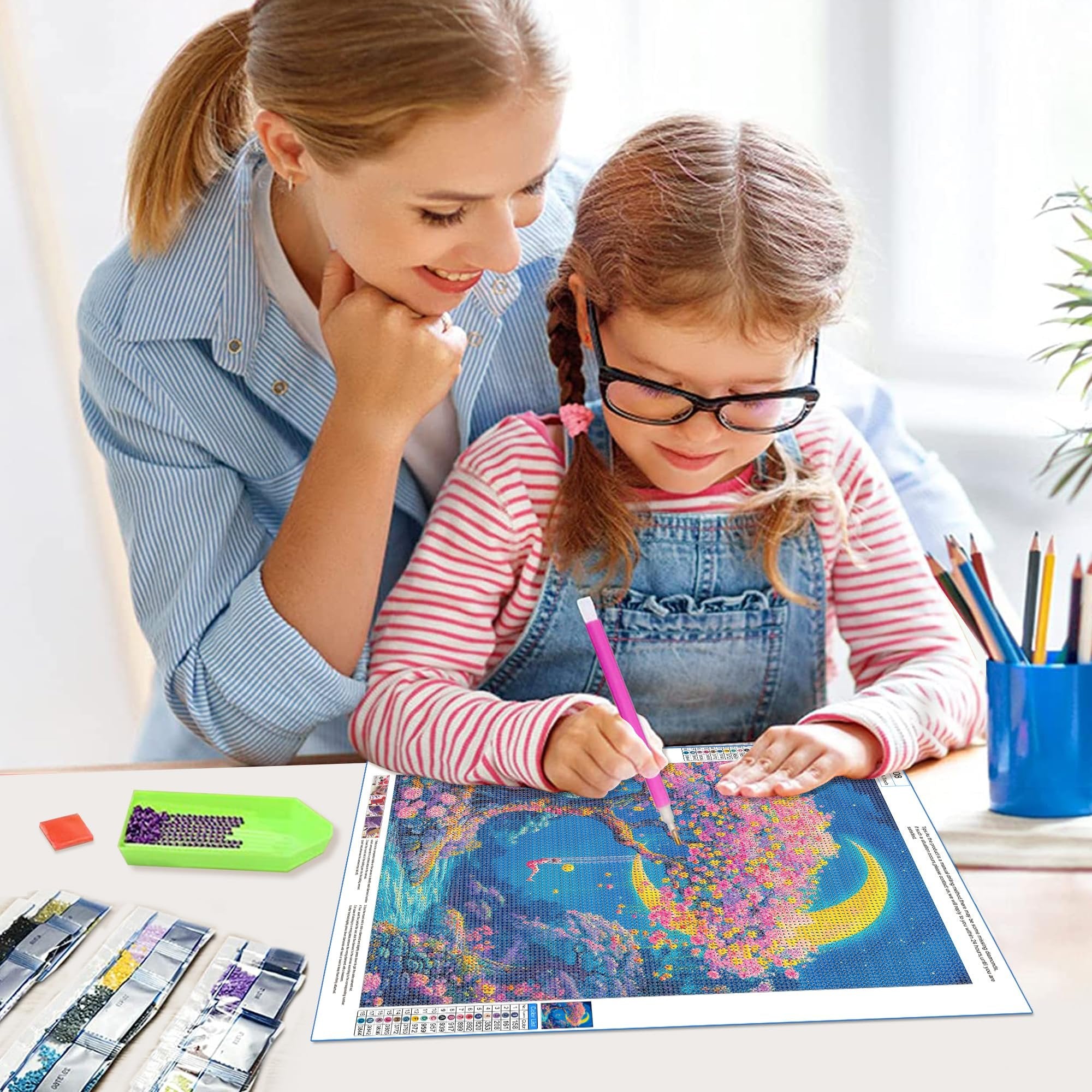 Mother and daughter doing a diamond painting kit of a moonlit forest scene with a crescent moon and a swing.