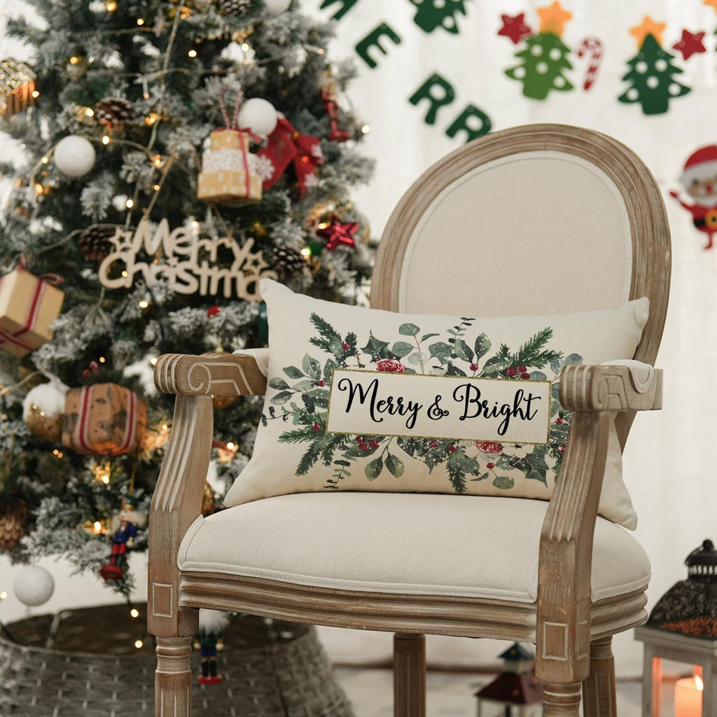 Christmas pillow cover with eucalyptus and mistletoe design on a chair next to a decorated Christmas tree.
