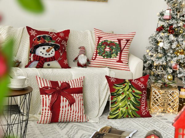 Four Christmas-themed throw pillow covers arranged on a couch next to a decorated Christmas tree.