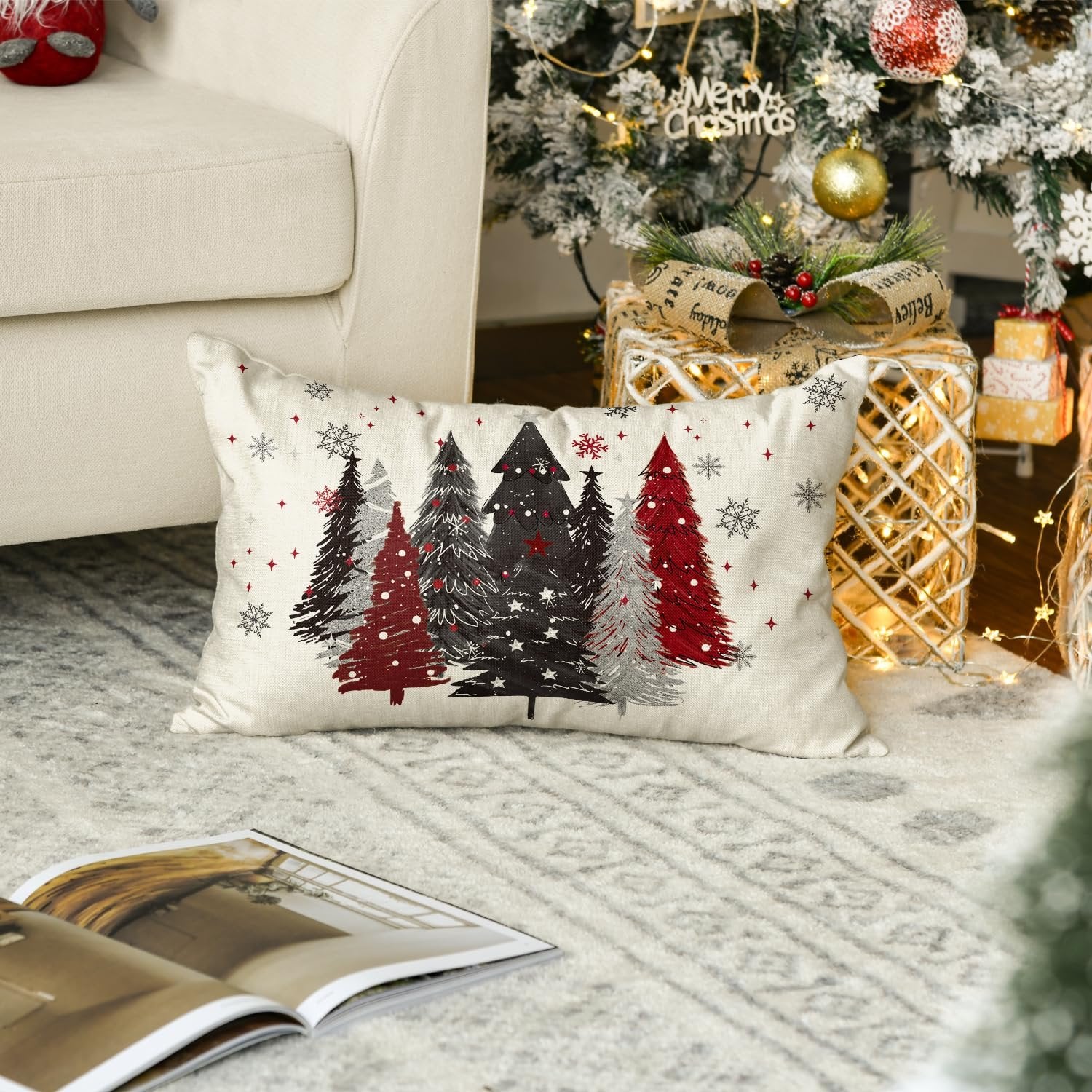 Rectangular Christmas throw pillow cover with red, black, and silver trees and snowflakes on a cream background, placed on a rug near a decorated Christmas tree.