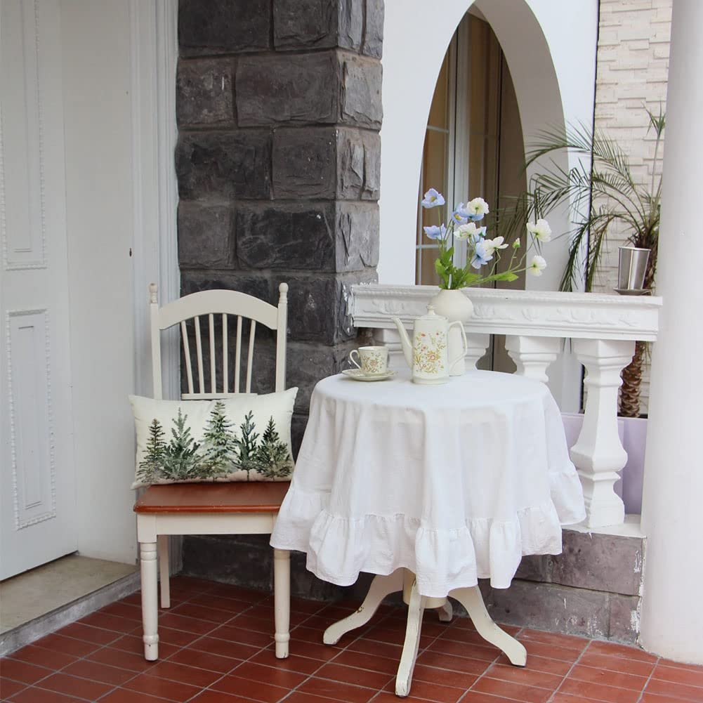 Lumbar pillow cover with a winter forest tree pattern resting on a chair next to a table with a white tablecloth and tea set.