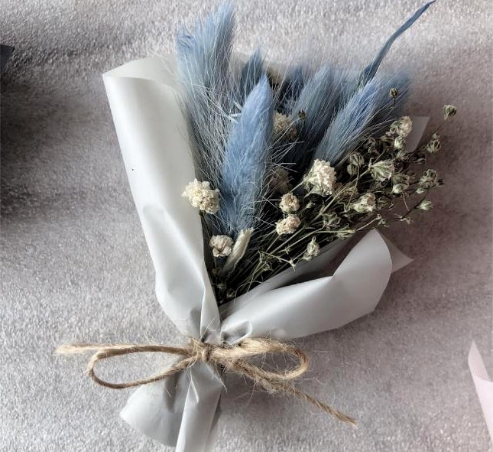 Bouquet of dried blue pampas grass and white baby's breath flowers wrapped in white paper and tied with twine.