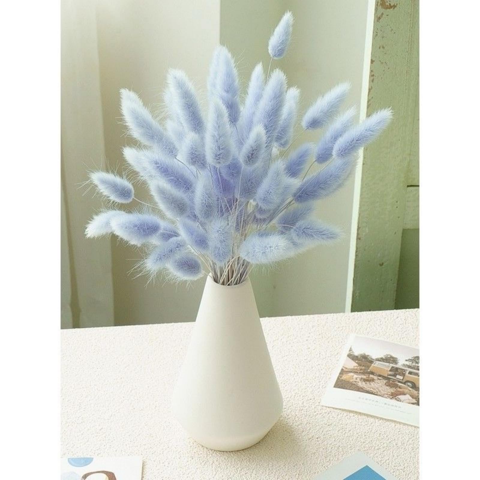 Bouquet of light blue bunny tail pampas grass in a white vase on a textured surface