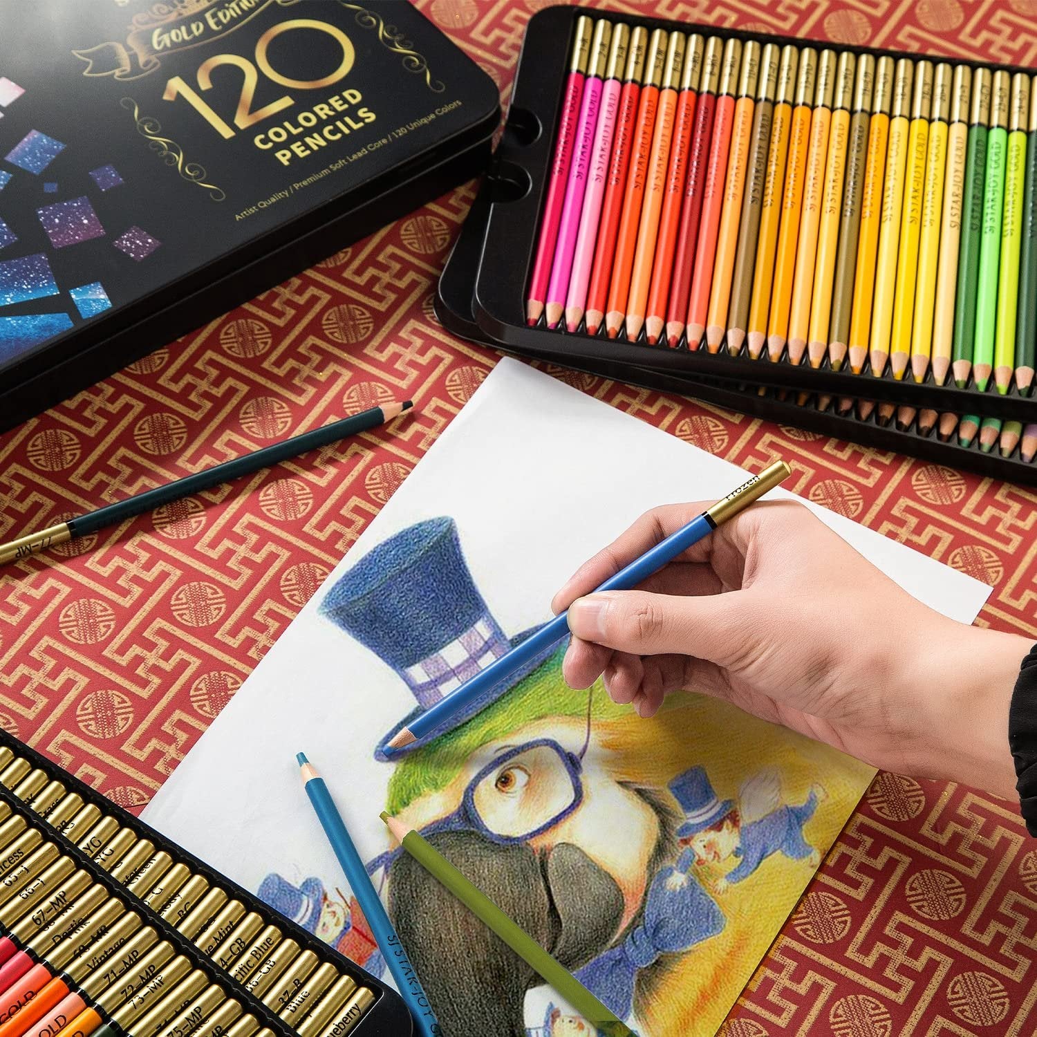 A hand holding a blue colored pencil and drawing on a paper featuring a parrot wearing a hat, with a tin of 120 colored pencils open nearby.