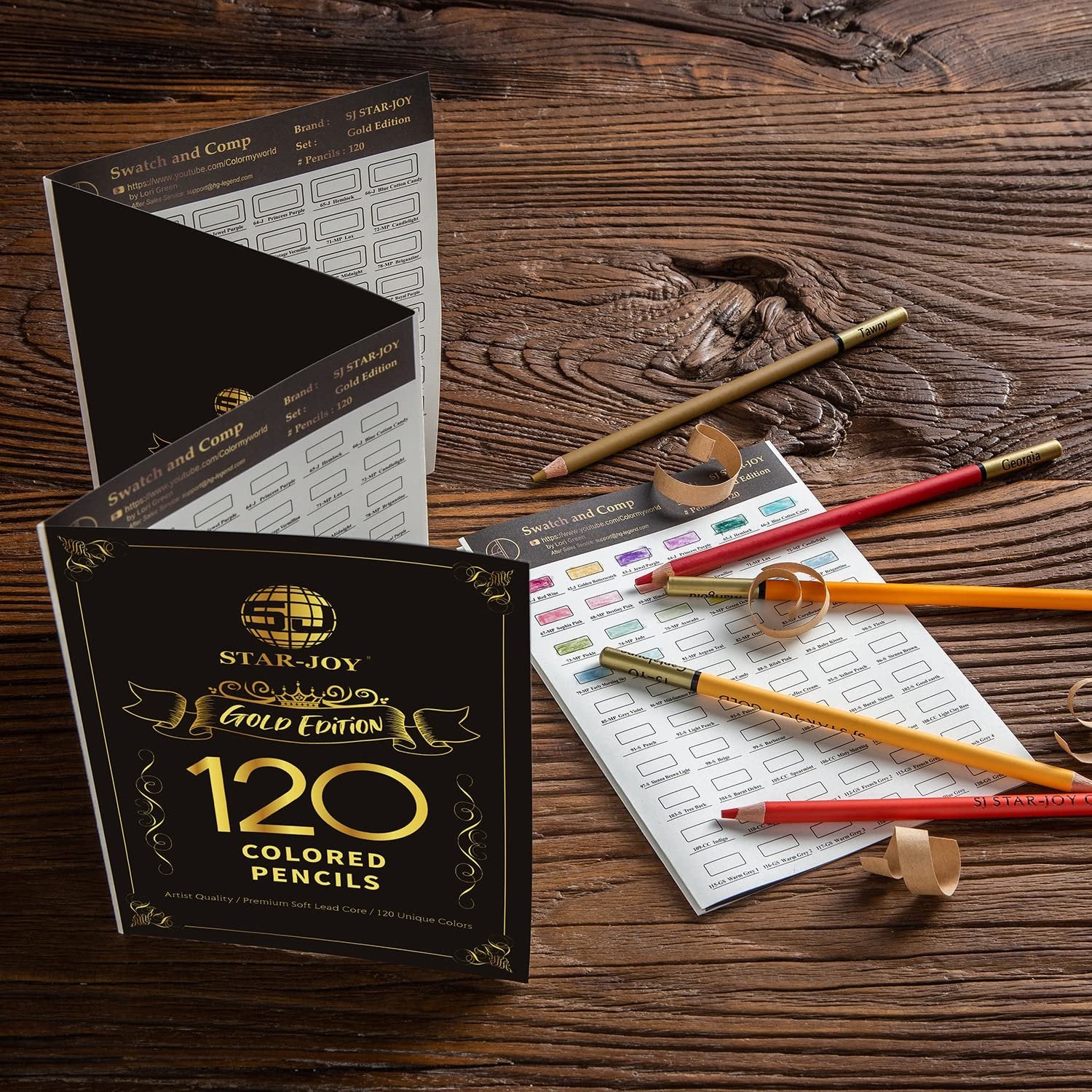 120 colored pencils laid out with swatch cards on a wooden surface, showing gold edition packaging.