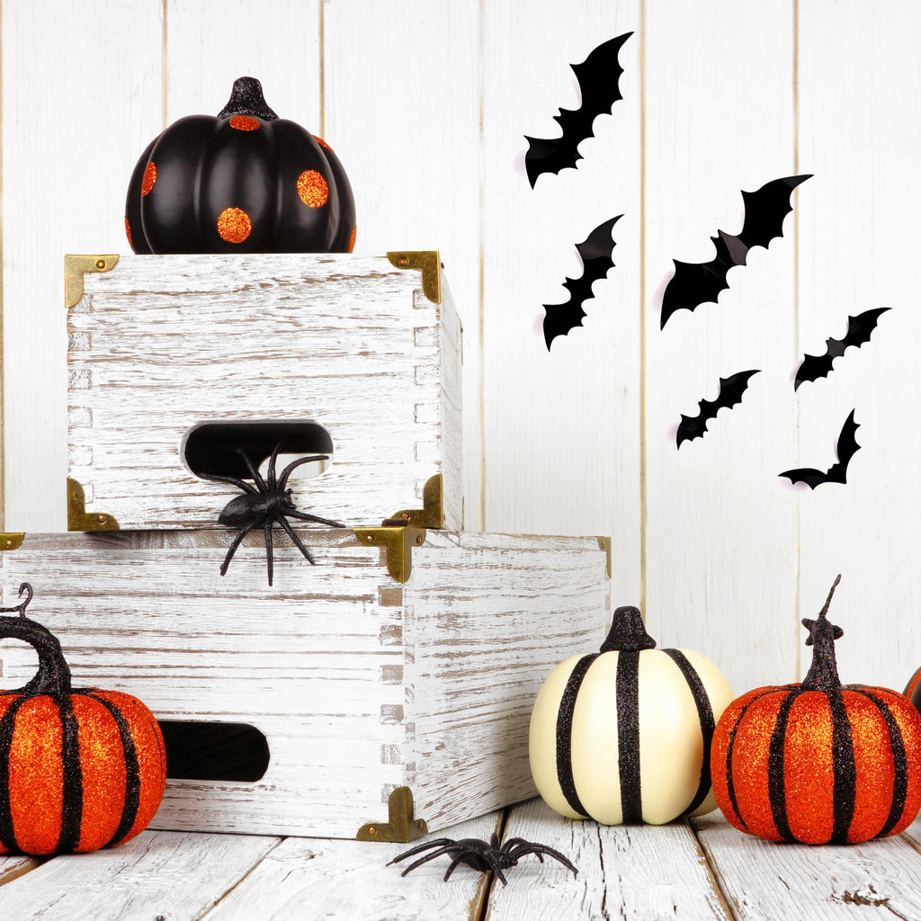 Halloween scene with decorative pumpkins, wooden crates, and black bat wall decals on a white wooden background.