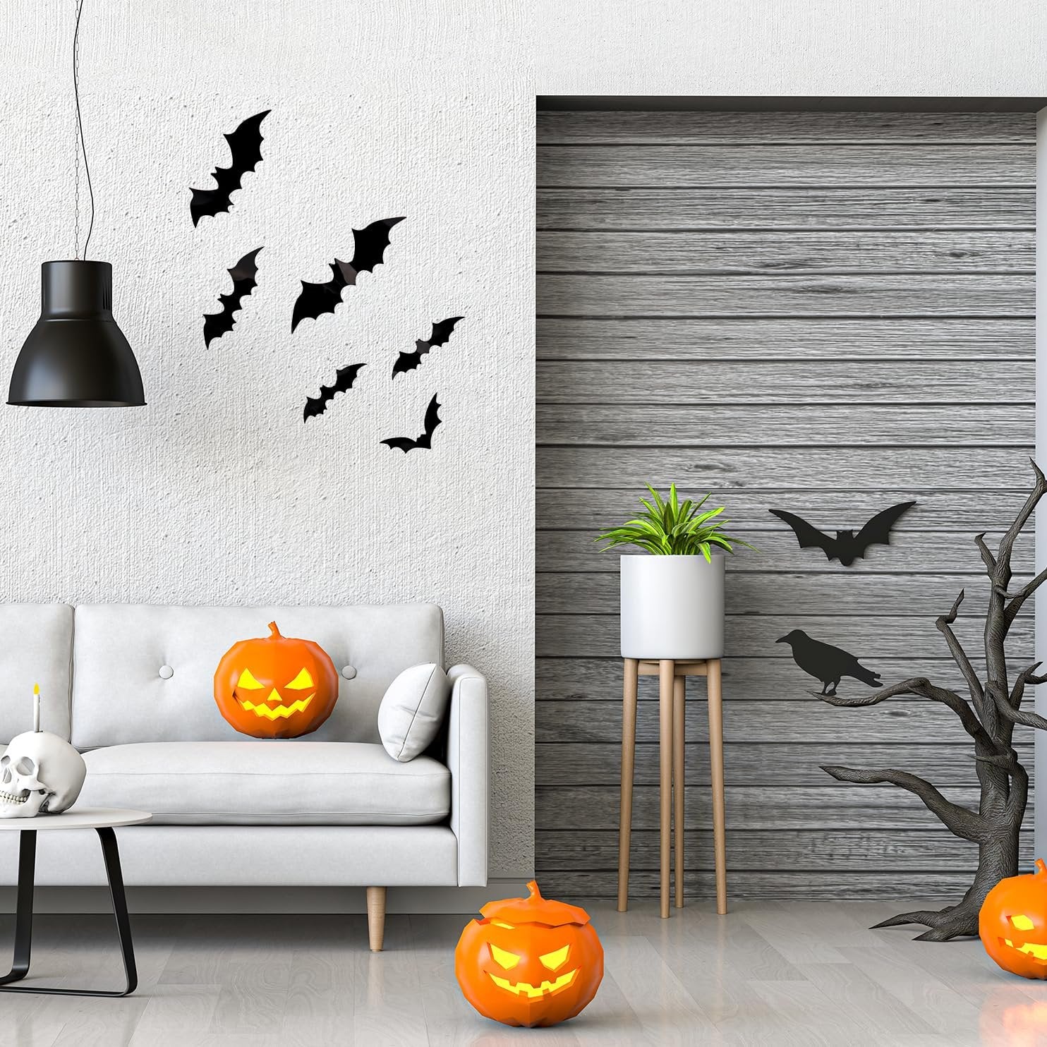 Halloween scene with black bat wall decals on a white wall, jack-o'-lanterns, a skull candle holder, and a plant on a stand.