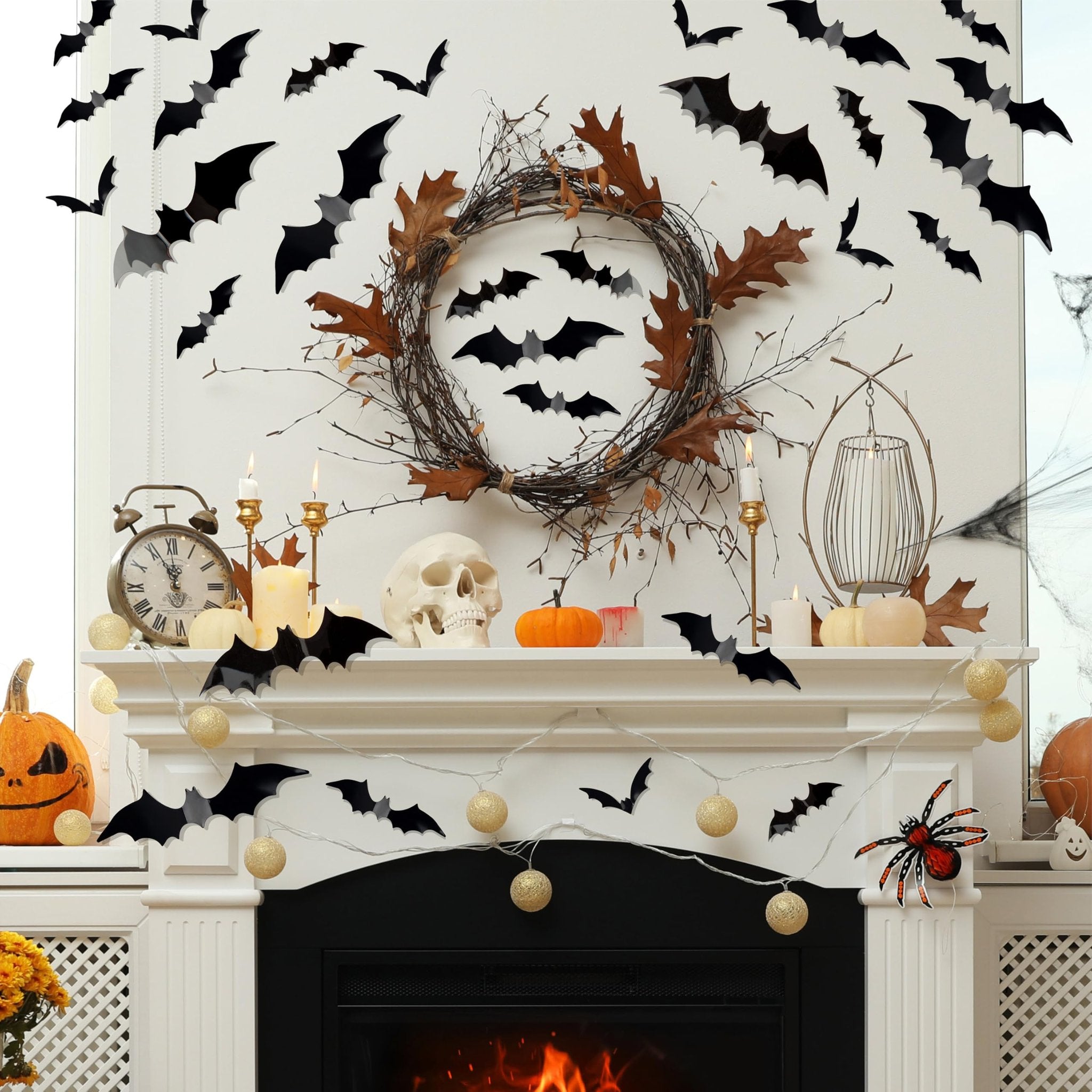 Halloween fireplace mantle decorated with black bat wall decals, a twig wreath, pumpkins, candles, and string lights.