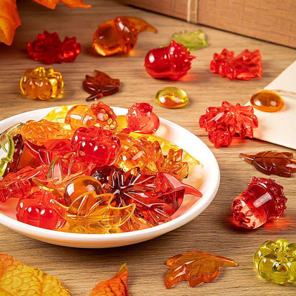 Acrylic fall vase filler set with pumpkins, leaves, and acorns in a white bowl on a wooden surface.
