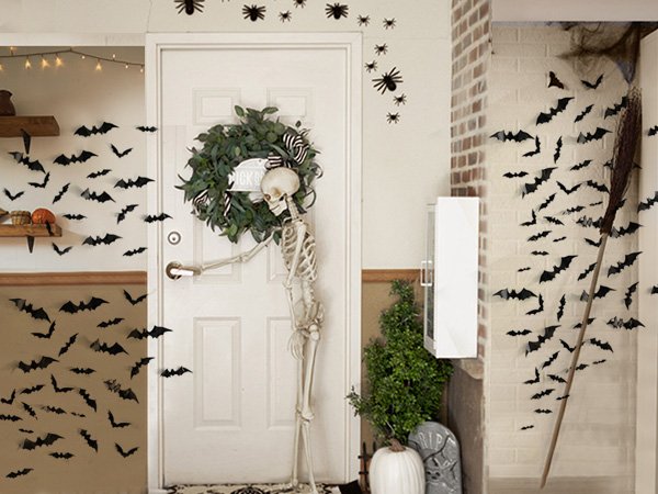 Halloween decorations including black 3D bat wall stickers, a skeleton, and a wreath on a door.