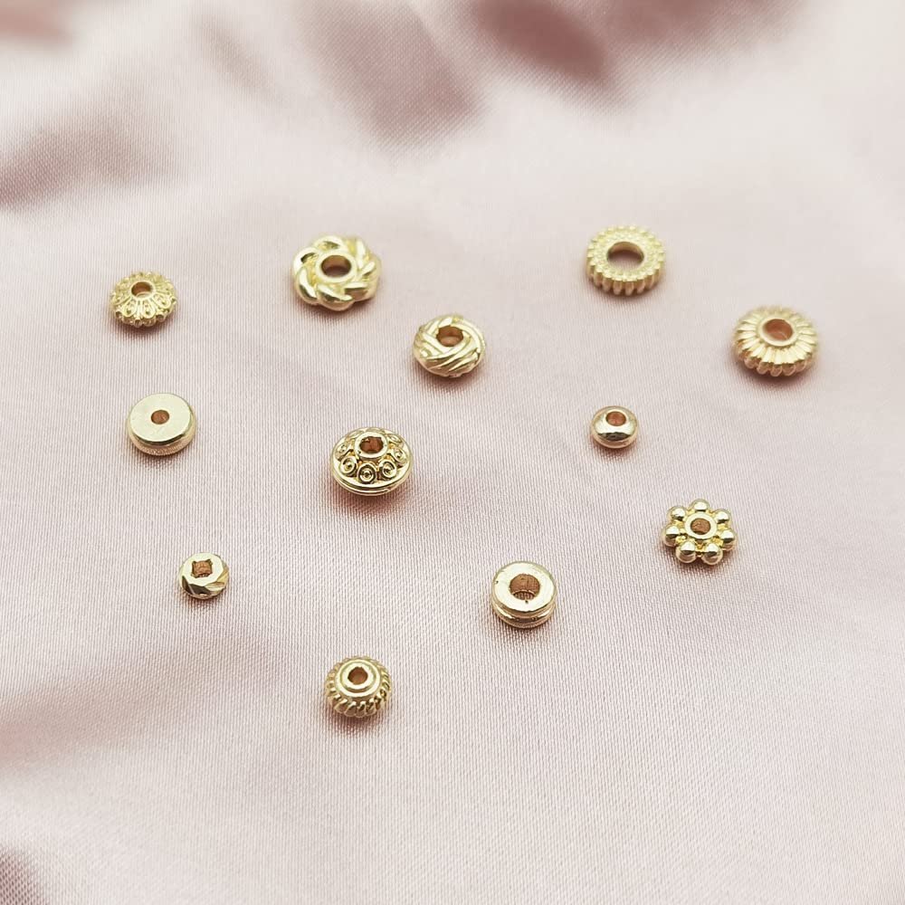 Assortment of gold-plated heishi and rondelle spacer beads for jewelry making, displayed on a pink satin background.