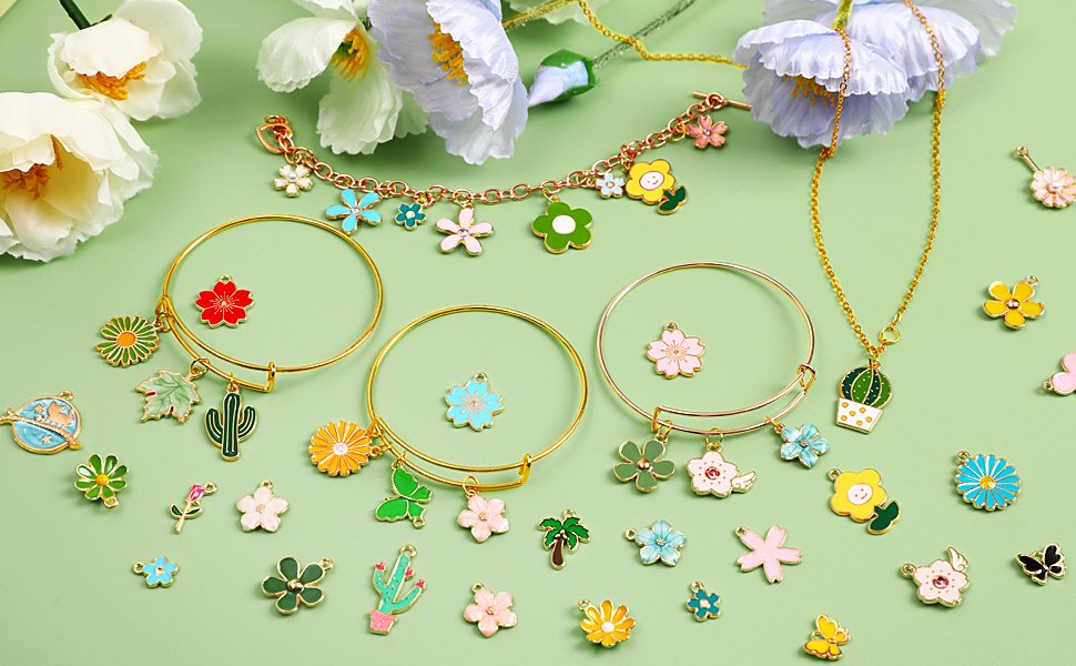Assortment of colorful enamel flower and nature charms scattered around bracelets and a necklace on a light green background with decorative flowers.