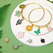 Spring flower and nature charms on gold bangles and scattered on a white surface, with a green fern leaf accent.