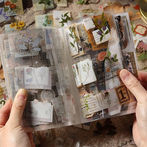 Hands holding an open binder of transparent nature-themed junk journal stickers with floral and butterfly designs.