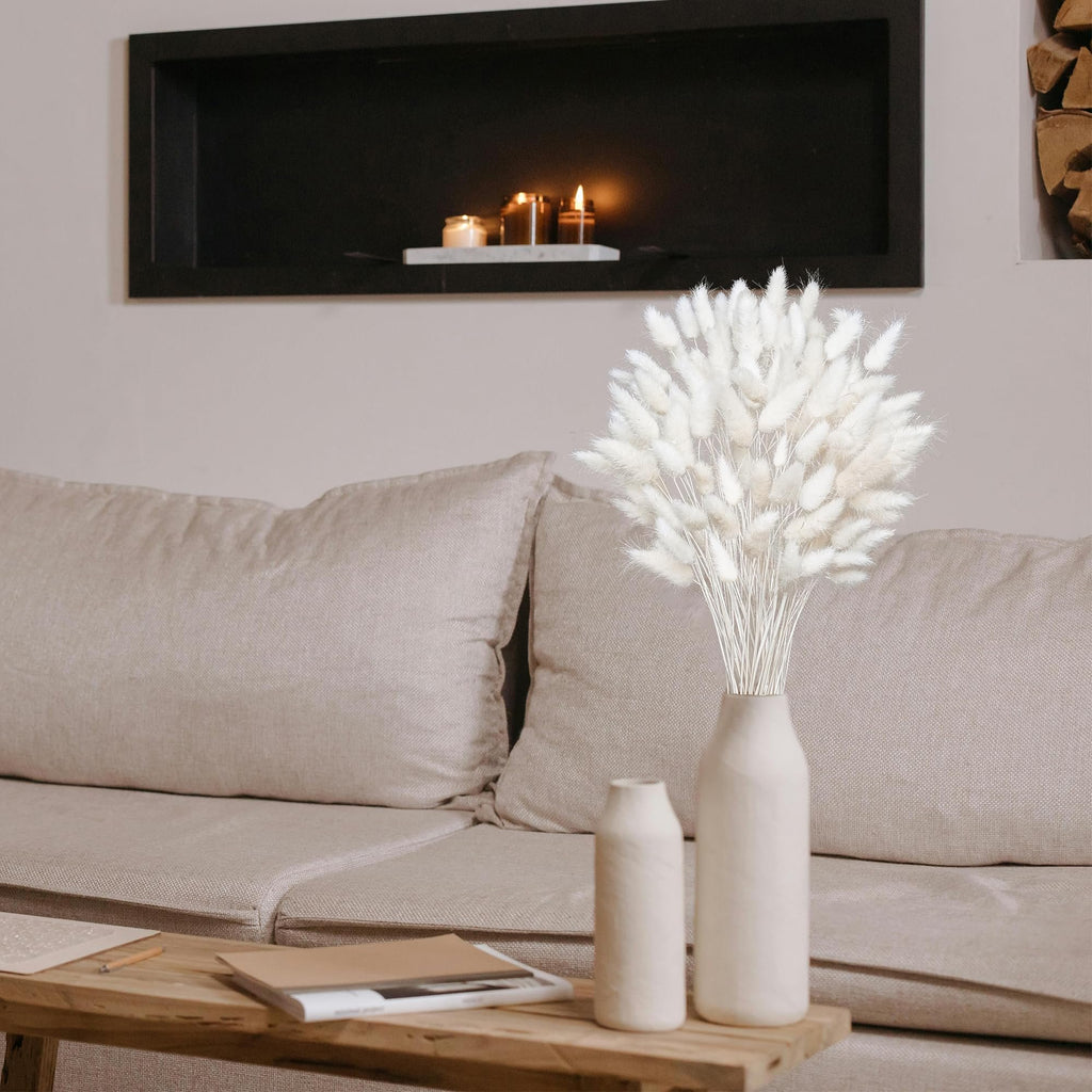 Bouquet of white dried pampas grass in a vase on a coffee table with books, next to a sofa.