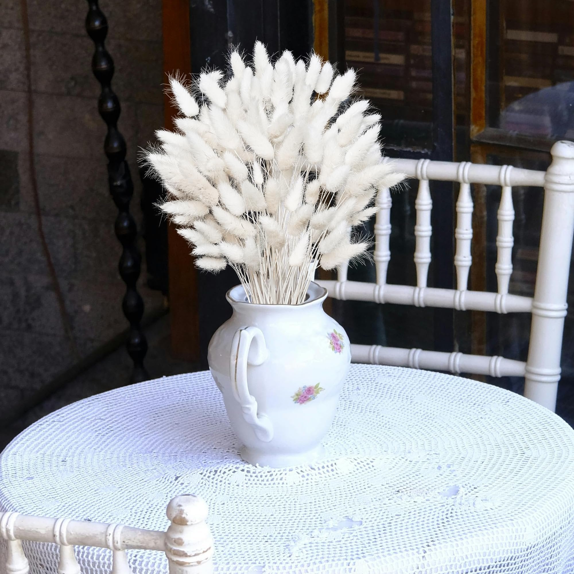 Bunch of white bunny tail grass stems in a decorative white vase on a lace tablecloth