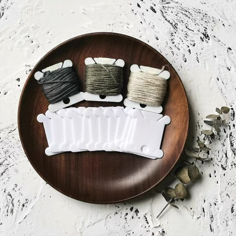 Three spools of embroidery floss on white bobbins arranged on a wooden plate with a row of empty white bobbins