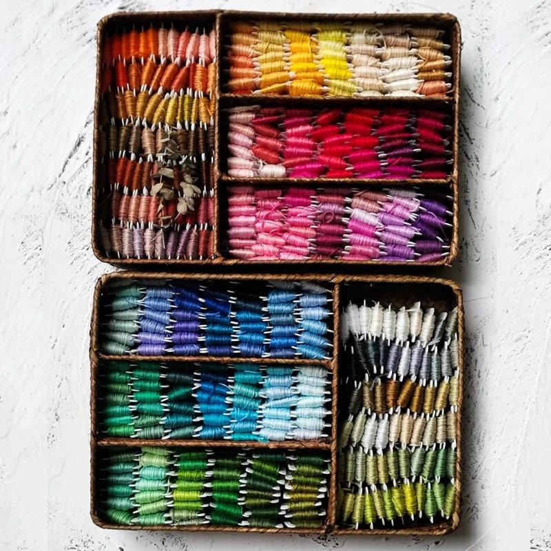 Two woven baskets filled with colorful embroidery floss bobbins organized by color, top-down view.