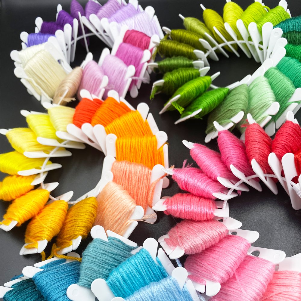 Assortment of colorful embroidery floss wound onto white plastic bobbins arranged in a spiral pattern on a black background.