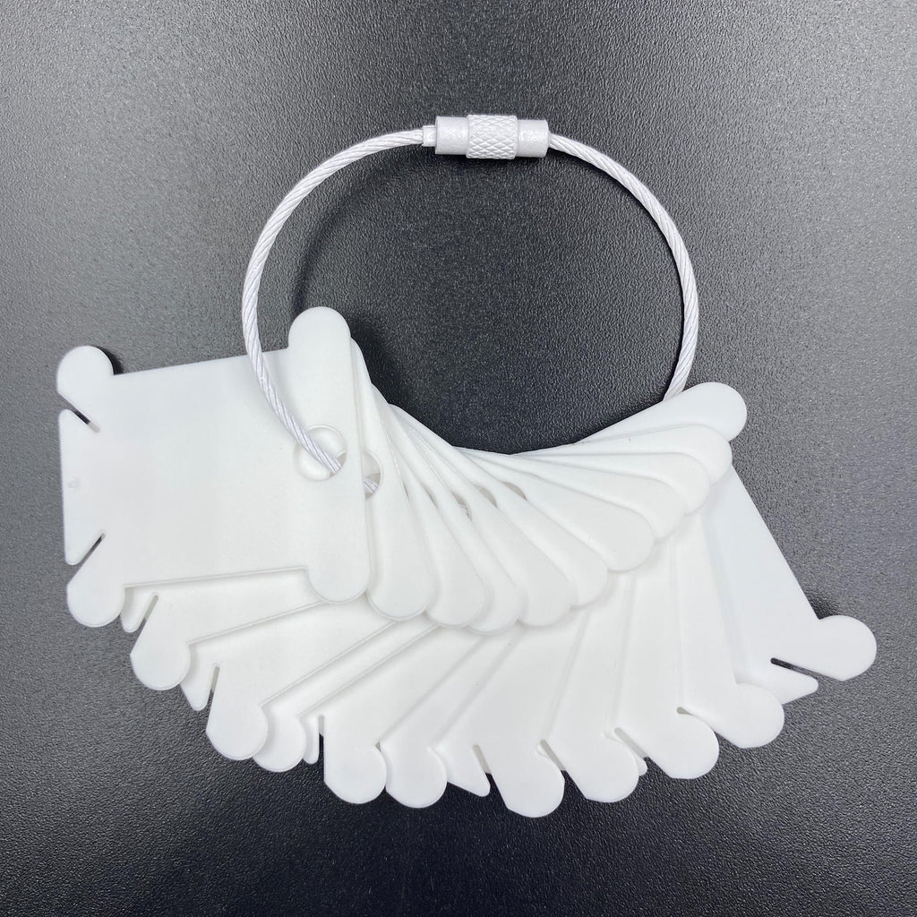 White plastic embroidery floss bobbins fanned out on a dark surface, attached to a metal ring.