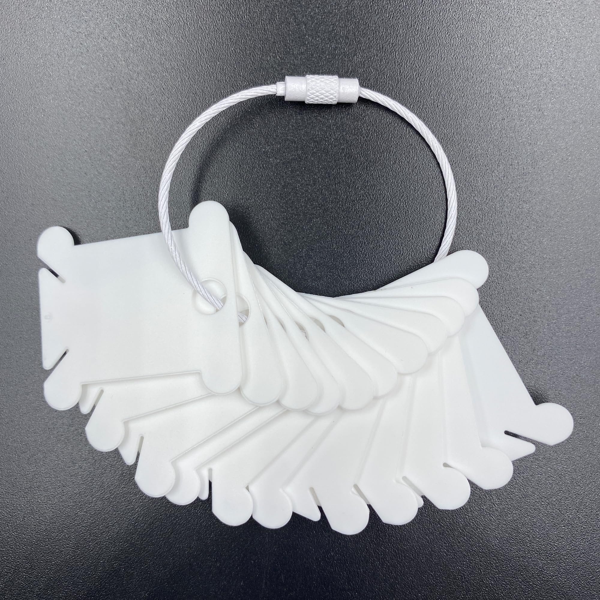 White plastic embroidery floss bobbins fanned out on a dark surface, attached to a metal ring.