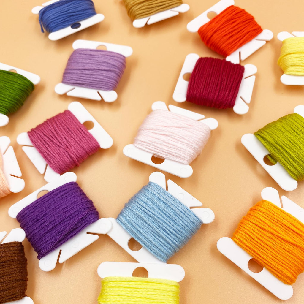 Assortment of colorful embroidery floss wound on white plastic bobbins, scattered on a peach background.