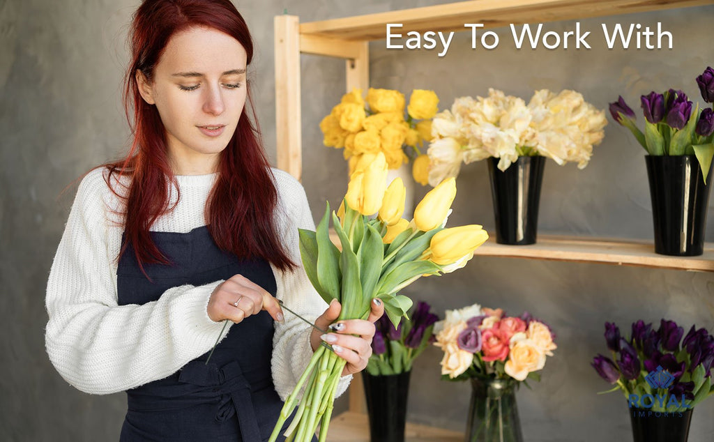 Florist using green paddle wire to tie a bouquet of yellow tulips, with other flowers on shelves.