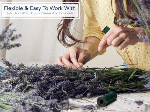 Hands wrapping green floral wire around a bundle of lavender stems on a wooden table.