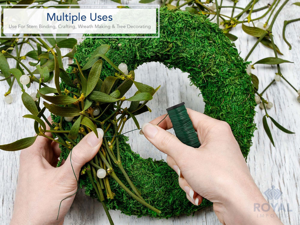 Hands using green paddle wire spool to attach mistletoe to a moss wreath for crafting.