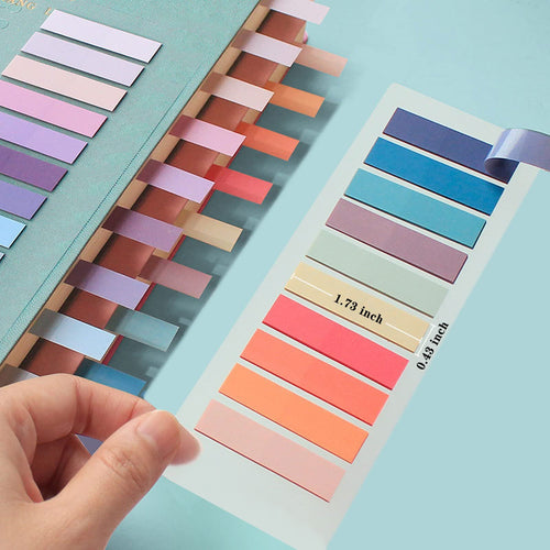 Hand placing colorful sticky note tabs into a planner, with a sheet of tabs showing dimensions.